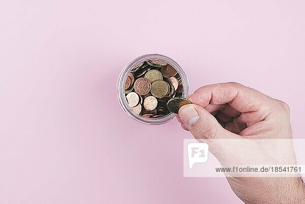 Ansicht von oben  wie eine Hand eine Münze in ein mit Kleingeld gefülltes Glas legt