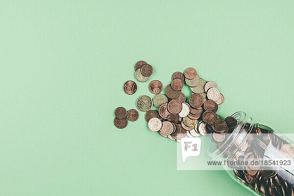 Blick von oben auf Euro-Kleinmünzen  die aus einem Glasgefäß auf grünem Hintergrund herausfallen