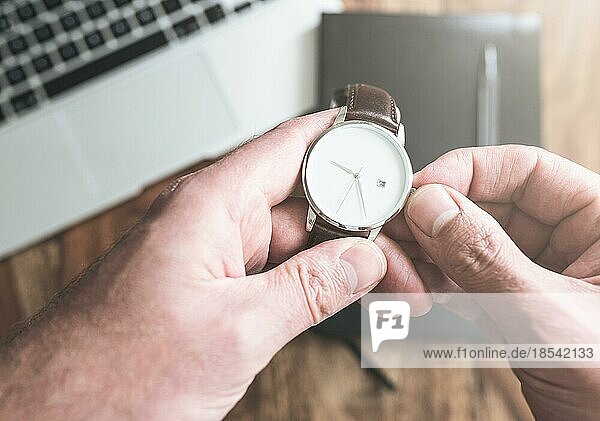 Mann stellt seine Armbanduhr gegen Laptop und Organizer auf einem Holztisch