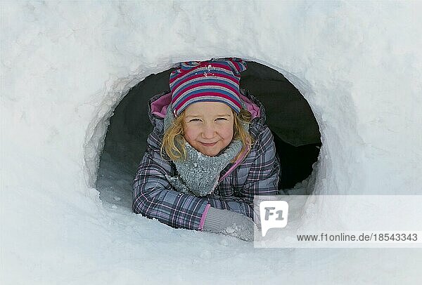 Mädchen schaut aus einer Schneehöhle heraus