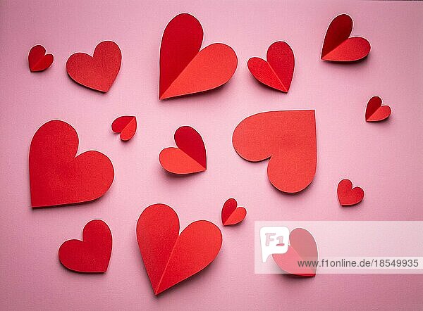 Rote Herzen aus Papier geschnitten auf rosa Hintergrund  Papier Handwerk OrigamiStil von oben. Romantische Valentinstag Hintergrund und Liebe Konzept. Verschiedene Größe rote Herzen Draufsicht  Papier Kunst Design