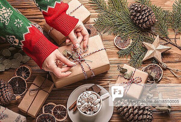 Weihnachten flach legen mit weiblichen Händen binden ein Band auf ein Geschenk  Geschenkboxen Tannenbaum Zweig auf hölzernen Hintergrund. Wrapping Xmas Geschenk Draufsicht  gemütliche festliche Zusammensetzung