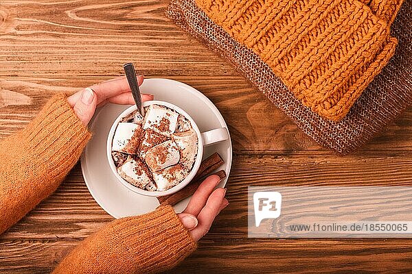 Gemütliche Winter flach legen  weibliche Hände halten Tasse mit heißer Schokolade oder Kakao mit Marshmallow und Stapel von warmen gestrickte Kleidung auf Holz rustikalen Hintergrund. Gemütlich und weich Winter oder Herbst Konzept