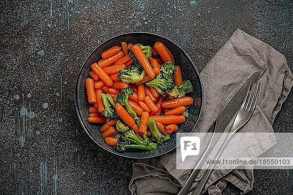 Gesunde Ernährung gedünstetes Gemüse Salat mit Baby Karotte und Brokkoli in der Schüssel Draufsicht auf Stein Hintergrund  sauberes Essen und Diäten Beilage gut für Gewichtsverlust