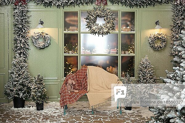 Weihnachtsatelierdekoration draußen in Grüntönen mit einer Bank und Plüschtieren in der Nähe der Café-Bäckerei  Tür  Kränze  Laternen  Girlande  Glasvitrine mit Lebkuchen  Fenster und viele Tannenbäume im Schnee