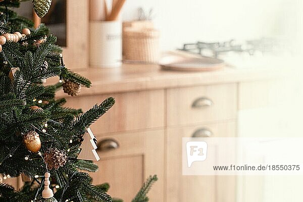 Nahaufnahme von dekoriert mit Holzspielzeug und Girlande großen schönen Weihnachtsbaum auf hellen Licht festliche moderne Küche mit Herd im skandinavischen Stil  Platz für Text