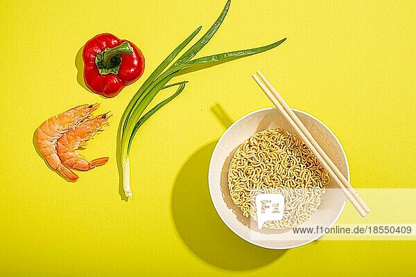 Flat Lay Draufsicht Lebensmittel Zusammensetzung mit ungekochten asiatischen schnellen Nudeln in Schüssel mit Zutaten für das Kochen Garnelen  Gemüse und grüne Zwiebel auf leuchtend gelbes Papier minimalen Hintergrund