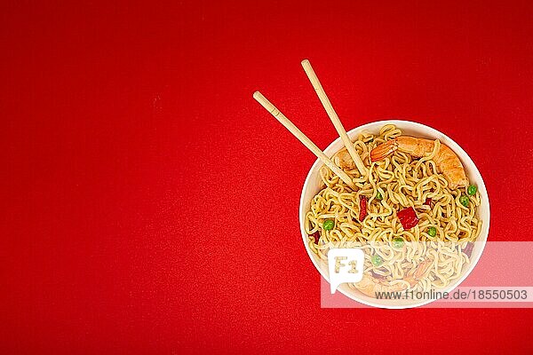 Asiatische chinesische Nudeln in der Draufsicht mit Garnelen und Gemüse in weißer Schüssel mit Holzstäbchen auf rotem minimalem Papierhintergrund  minimales Foodphoto Konzept  Platz für Text