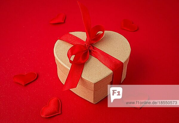 Schöne minimale verpackt Geschenk-Box in Herzform mit roter Schleife Band auf rotem Hintergrund und kleine gepolsterte Herzen Draufsicht flach legen  Geschenk für Saint Valentine Tag  Liebe und Beziehung Konzept