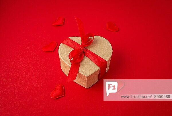 Schöne minimale verpackt Geschenk-Box in Herzform mit roter Schleife Band auf rotem Hintergrund und kleine gepolsterte Herzen Draufsicht flach legen  Geschenk für Saint Valentine Tag  Liebe und Beziehung Konzept