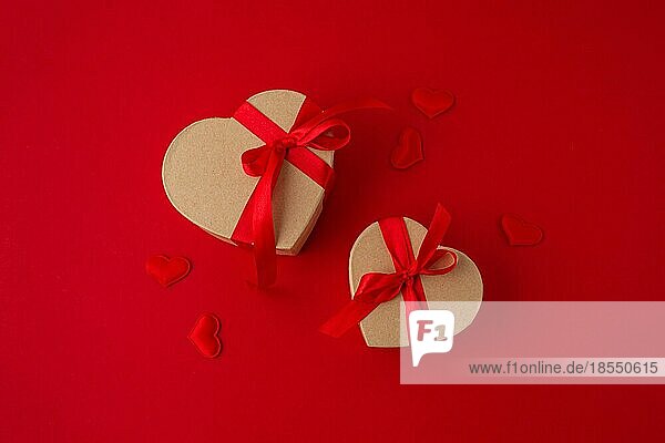 Zwei verpackte Geschenk-Boxen in Herzform mit roter Schleife Band auf rotem Hintergrund und kleine gepolsterte Herzen Draufsicht flach legen  Geschenke für Saint Valentine Tag  Liebe und Beziehung Konzept