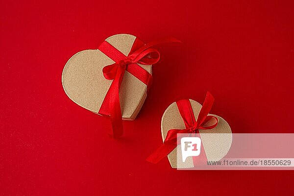 Zwei verpackte Geschenk-Boxen in Herzform mit roter Schleife Band auf rotem Hintergrund Draufsicht flach legen  Geschenke für die Feier Saint Valentine Tag  Liebe und Beziehung Konzept