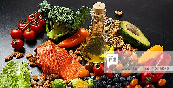 Gesunde Ernährung und Ernährung Lebensmittel reich an Vitaminen und Omega-3-Konzept  sortiertes frisches Gemüse  grüner Salat  Obst  Fisch Lachs  Nüsse  Blaubeeren  Flasche Olivenöl auf schwarzem Kreidebrett Hintergrund