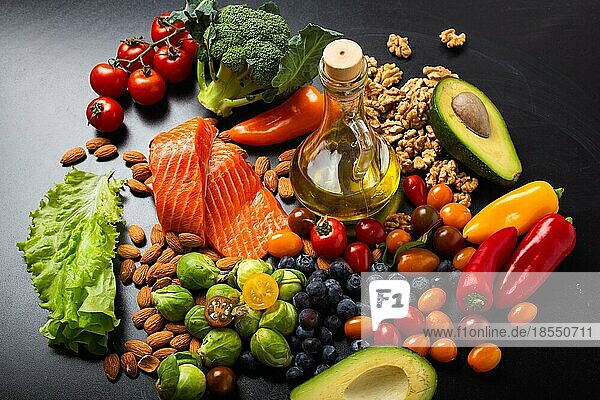 Gesunde Ernährung und Ernährung Lebensmittel reich an Vitaminen und Omega-3-Konzept  sortiertes frisches Gemüse  grüner Salat  Obst  Fisch Lachs  Nüsse  Blaubeeren  Flasche Olivenöl auf schwarzem Kreidebrett Hintergrund
