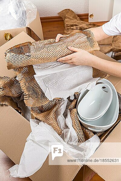 Detail einer Frau  die zerbrechliche Gegenstände mit zerknittertem Packpapier verpackt. Konzept des Umzugs in oder aus