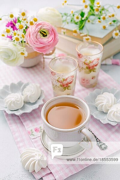 Tasse Tee  kleine Baiser Kekse und Bücher mit schönen zarten Blüte von frischen Schnittblumen im Hintergrund