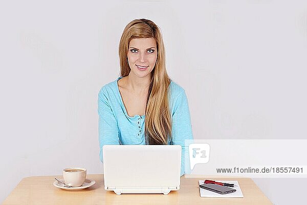 Junge Frau sitzt am Schreibtisch im Home Office mit Laptop und Kaffee