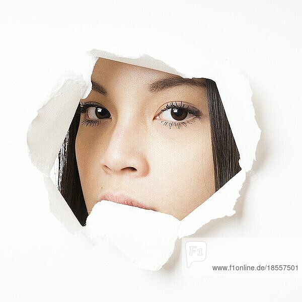 Junge asiatische Frau späht durch ein Loch in der Papierwand