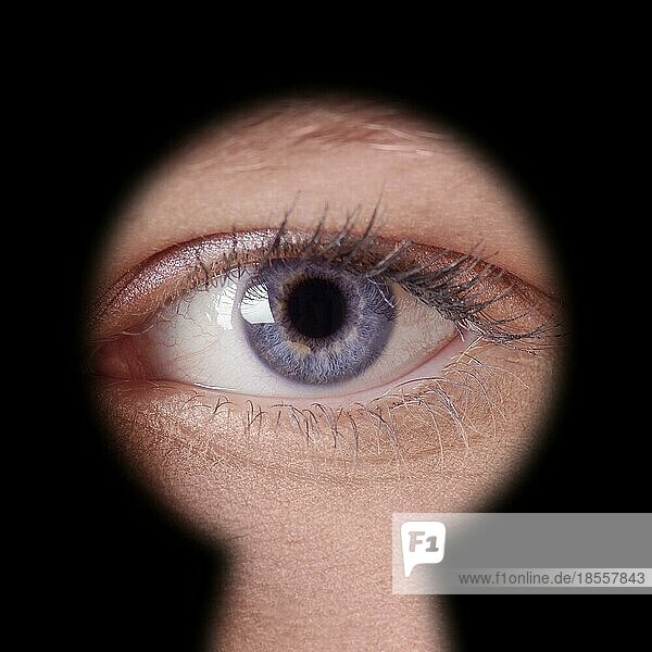 Nahaufnahme eines menschlichen weiblichen blaün Auges  das durch ein Schlüsselloch schaut