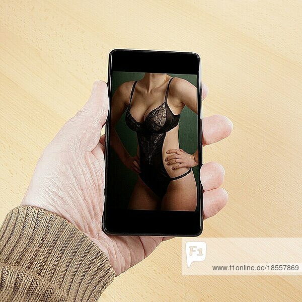 Männliche Hand  die ein Smartphone hält  das ein sexy Foto eines weiblichen Körpers in Dessous zeigt