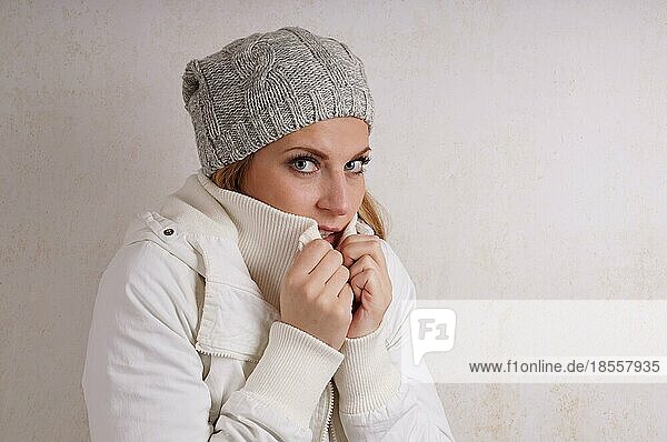 young woman wearing woolen hat and winter jacket is freezing