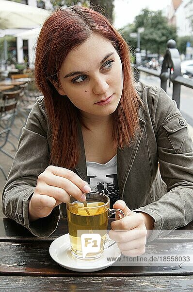 Junge Frau trinkt Tee in einem Straßencafé