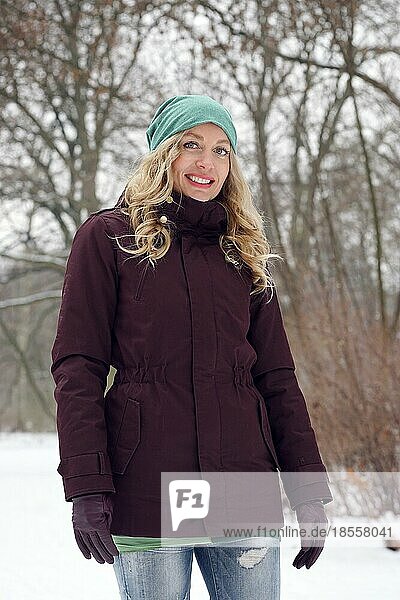 Blonde Frau in verschneitem Wald in Winterkleidung stehend