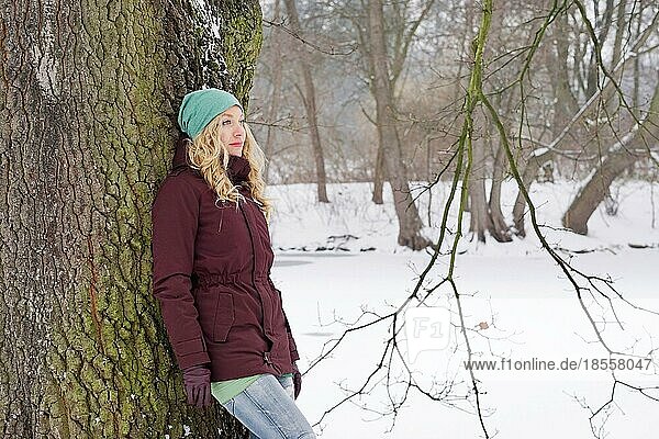 pensive woman leaning against birch tree in snow covered winter landscape