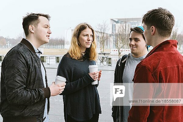 group of teenage friends having a conversation while standing together on city street holding coffee cups