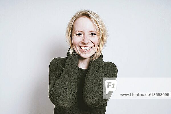Porträt einer blauäugigen  blonden  fröhlichen jungen Frau mit breitem Lächeln aus Deutschland  die vor einer Innenwand mit Kopierraum steht