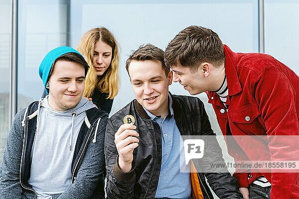 young man showing bitcoin coin to his intrigued group of friends  cryptocurrency hype concept