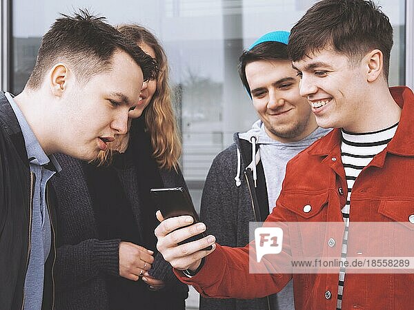 young man showing something funny on his smartphone to a group of teenage friends  focus on hand holding mobile phone  matte filter