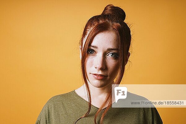 Coole junge Frau mit roten Haaren unordentliche Brötchen Frisur und lose Strähnen auf der Vorderseite gegen gelb orange Farbe Hintergrund mit opy Raum