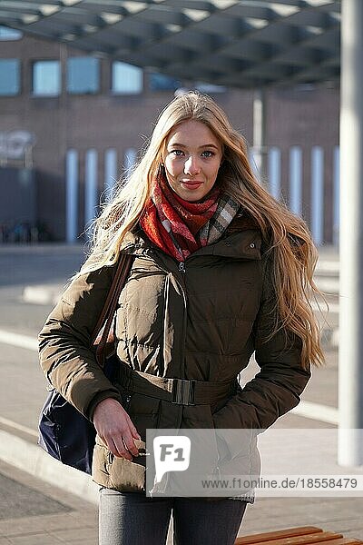 Straße Stil Mode Porträt der jungen Frau wartet am Busbahnhof an einem sonnigen Tag im Winter