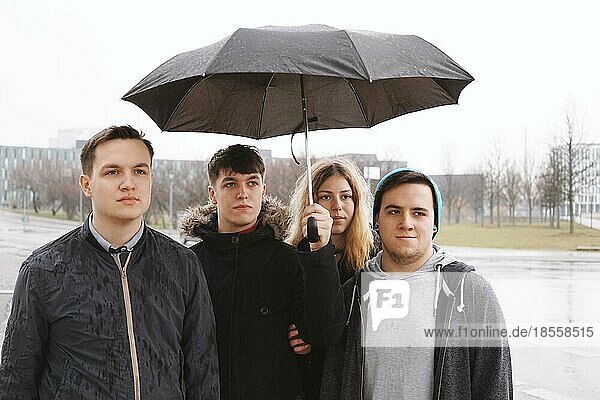 group of young urban teenage friends under one umbrella in the rain