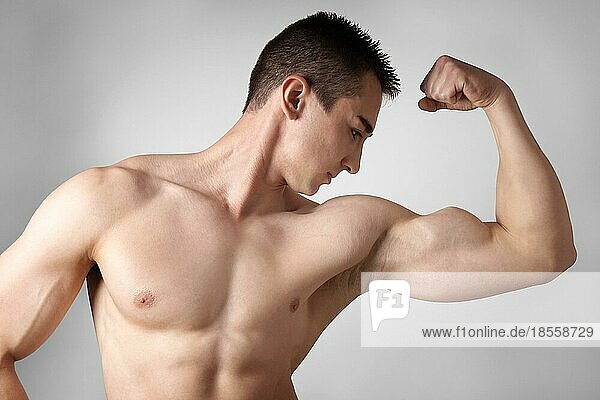 Hemdloser junger Mann  der seine Bizepsmuskeln beugt und seine Stärke zeigt