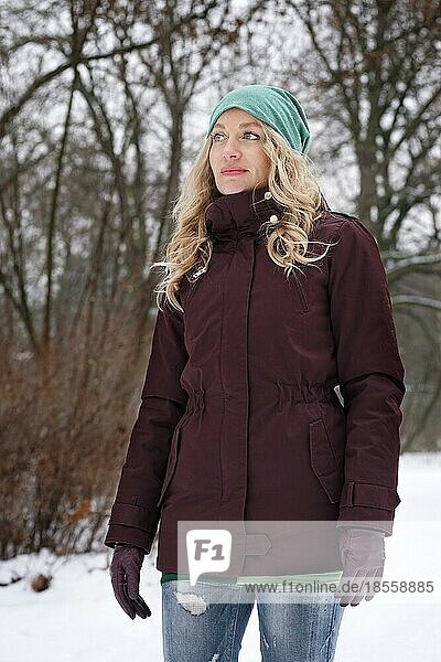 Blonde Frau im verschneiten Wald im Winter stehend