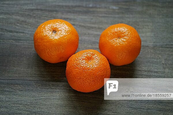 Drei ganze Clementinen oder Mandarinen auf einem rustikalen Holztisch mit geringer Tiefenschärfe