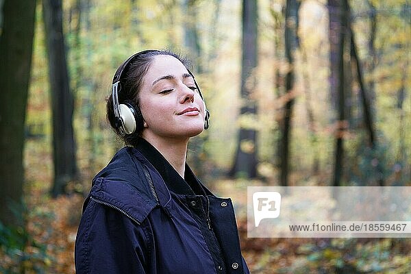 Junge Frau in den 20ern hört Musik mit kabellosen Kopfhörern im Wald - candid outdoor lifestyle im Herbst - mit Kopierraum