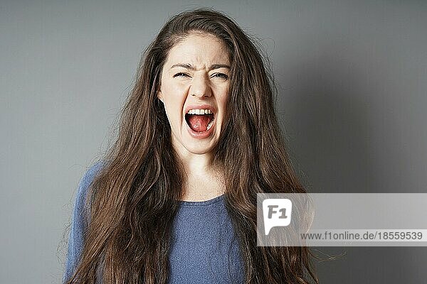 Wütende hysterische junge Frau schreit und schreit - grauer Hintergrund mit Kopierraum