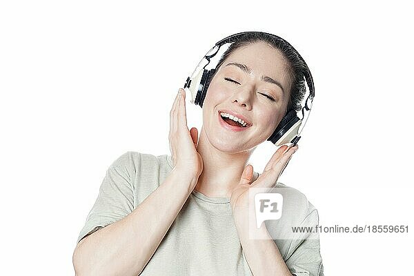 Glückliche junge Frau in den 20ern  die mit drahtlosen Kopfhörern Musik hört - Mädchen vor weißem Hintergrund
