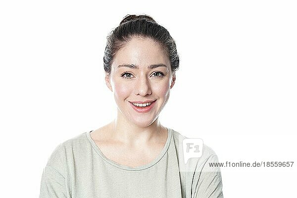 Fröhliche junge Frau in den 20ern mit natürlichem Make-up und brünettem Haarknoten lächelnd - vor weißem Hintergrund