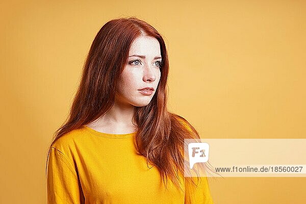 Junge Frau mit ausdruckslosem Gesicht  die über einen Gedanken nachdenkt - gelber Hintergrund mit Leerzeichen