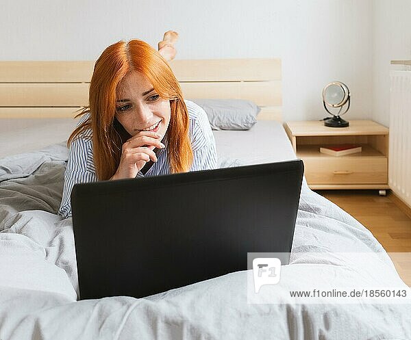happy young woman lying with laptop on bed and relaxing at home