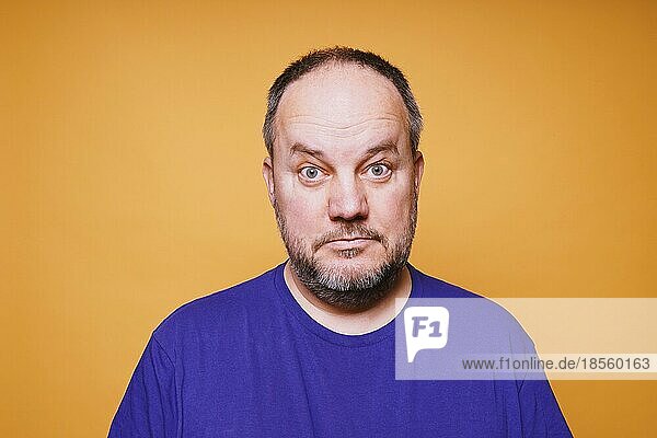 Porträt eines erwachsenen Mannes mit verblüfftem Gesichtsausdruck vor orangefarbenem Studiohintergrund - verwirrter Gesichtsausdruck