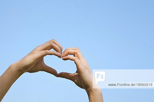 Weibliche Hände machen Herzform Zeichen oder Liebe Geste gegen klaren blaün Himmel mit Kopie Raum