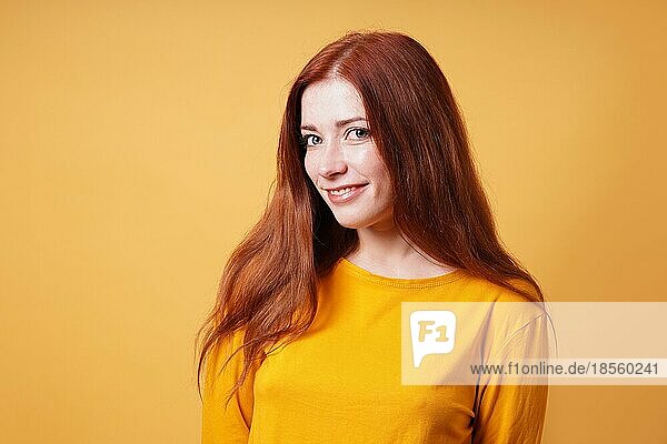 Glückliche junge Frau mit langen roten Haaren lächelnd - gelber farbiger Hintergrund mit Kopierraum