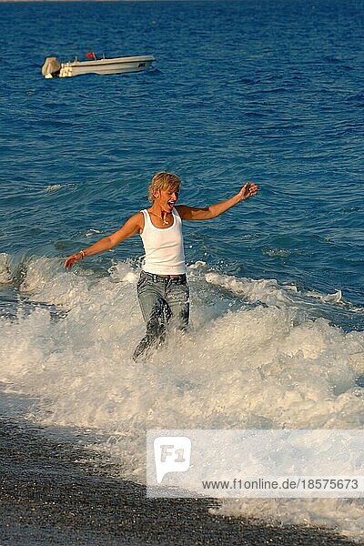 Junge Frau läuft in ärmelloses weißes Shirt und Jeans an schwarzer Strand von Ostatlantik durch Brandung Wellen Gischt  Teneriffa  Kanarische Inseln  Spanien  Europa