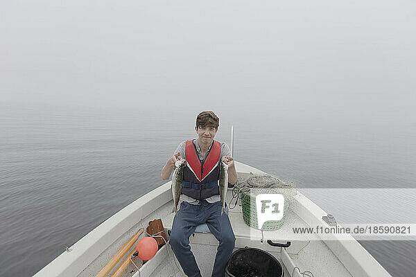 Boy (15-16) sitting in boat and holding fish