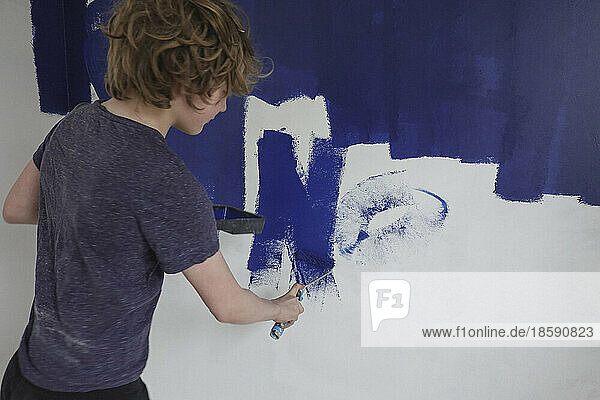 Boy painting wall with blue paint